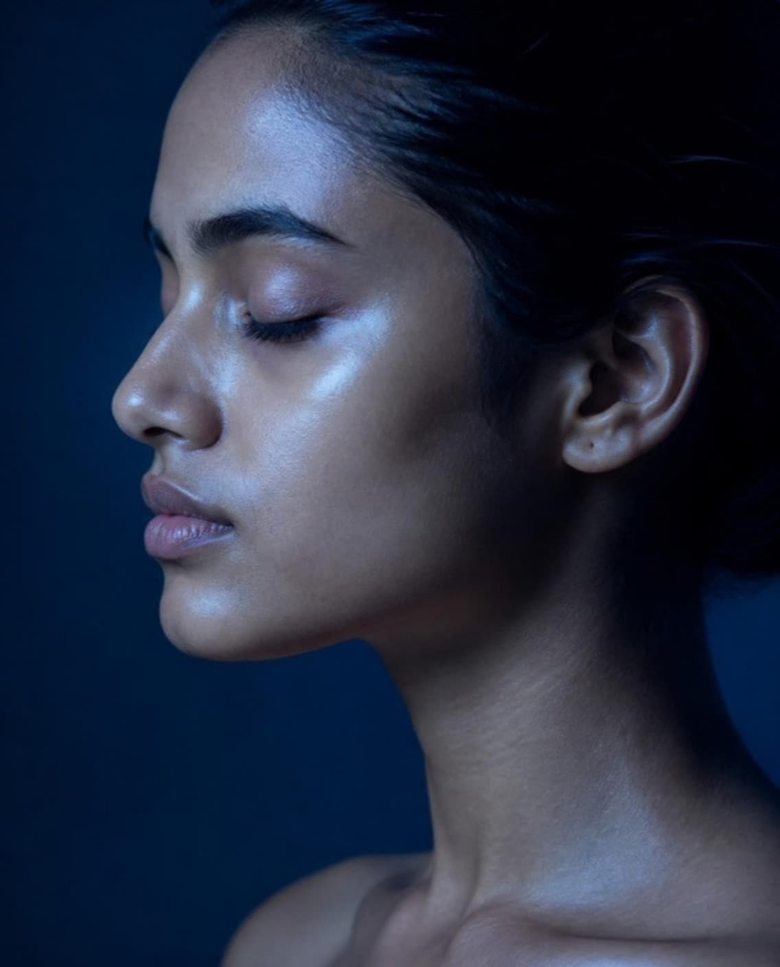 Side profile of a young woman, eyes closed, skin lit in cool blue light.